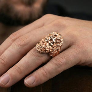 Rose gold plated Zeus ring on finger featuring ornate god face relief, refined men’s jewelry lifestyle wear shot