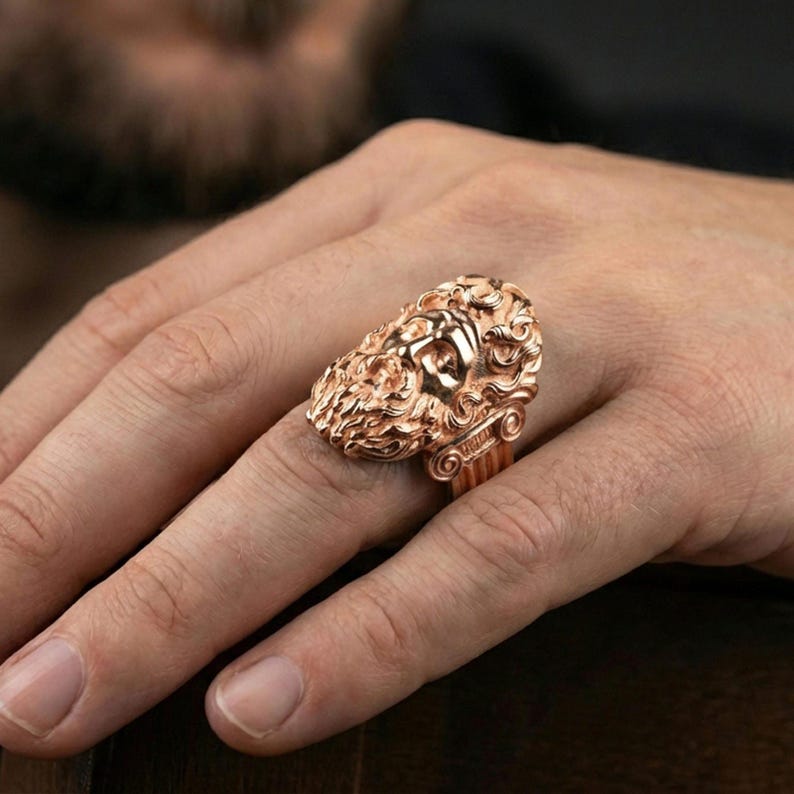 Rose gold plated Zeus ring on finger featuring ornate god face relief, refined men’s jewelry lifestyle wear shot