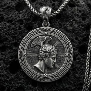 Oxidized Perseus coin pendant necklace on textured volcanic rock, centered close-up highlighting the Greek key border, winged helmet profile, and deep antique shadowed contrast.