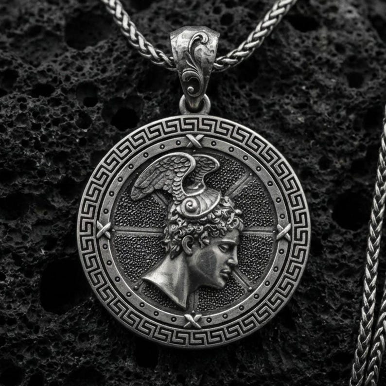 Oxidized Perseus coin pendant necklace on textured volcanic rock, centered close-up highlighting the Greek key border, winged helmet profile, and deep antique shadowed contrast.