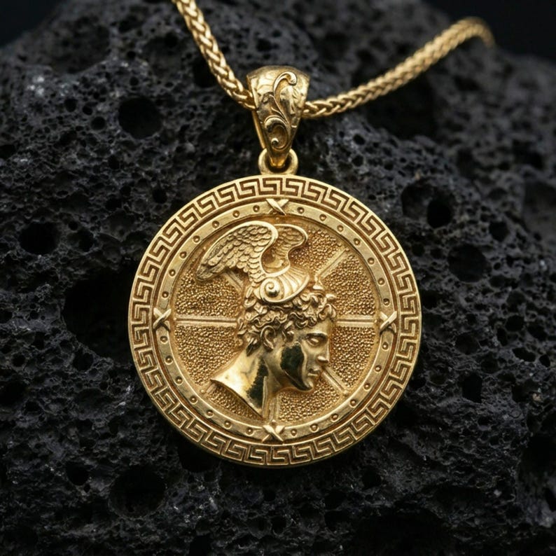Gold plated Perseus coin pendant necklace on textured volcanic rock, premium close-up with warm reflective shine across the winged helmet, facial relief, and raised meander frame.