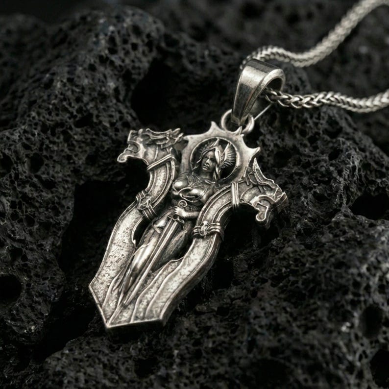 Oxidized gothic cross pendant necklace on textured volcanic rock, centered close-up highlighting the armored angel figure, sharp edges, and deep antique contrast.