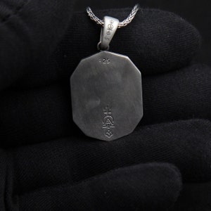 May include: Silver pendant with a geometric shape and a detailed design on the back. The pendant has a 925 stamp and a small inscription that reads "25".
