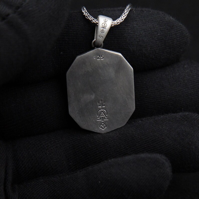 May include: Silver pendant with a geometric shape and a detailed design on the back. The pendant has a 925 stamp and a small inscription that reads "25".