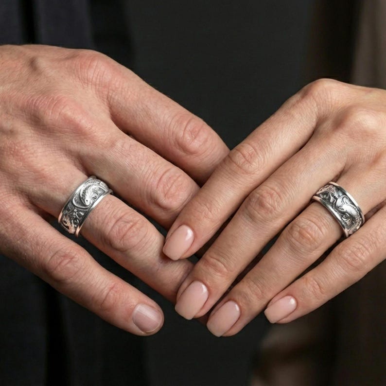 Polished silver dragon and koi fish wedding band on finger, crisp relief sculpture and textured backdrop, refined everyday wear close-up.