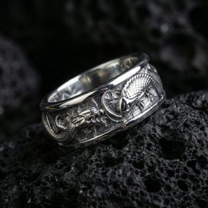 Polished silver dragon and koi fish wedding band on black volcanic stone, crisp sculpted relief with deep carved background, centered close-up studio lighting.