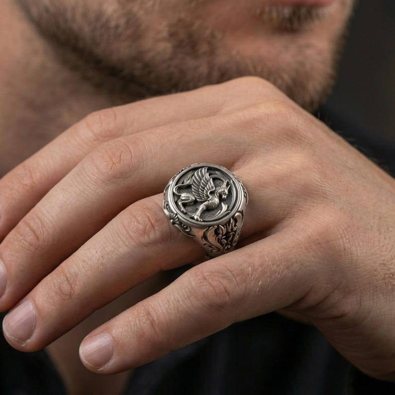 Oxidized sterling silver griffon ring worn on finger, bold mythical creature design with wings and lion body, masculine lifestyle hand shot