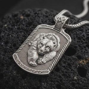 Polished sterling silver bear and cub necklace displayed on dark volcanic stone, highlighting the intertwined parent and cub portraits, realistic fur details, and rugged dog tag pendant.