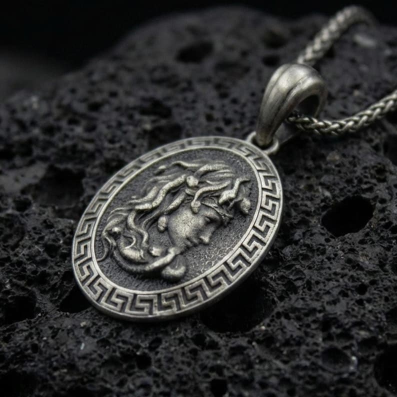 Oxidized 925 sterling silver Medusa coin pendant on volcanic rock, Greek key border medallion with raised goddess profile relief