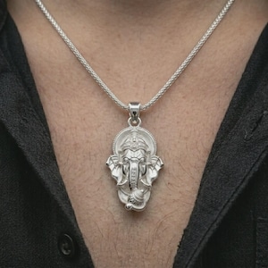 Polished silver Ganesha pendant necklace worn on the chest, masculine lifestyle shot highlighting the elephant god relief, ornate crown, and bright silver finish.