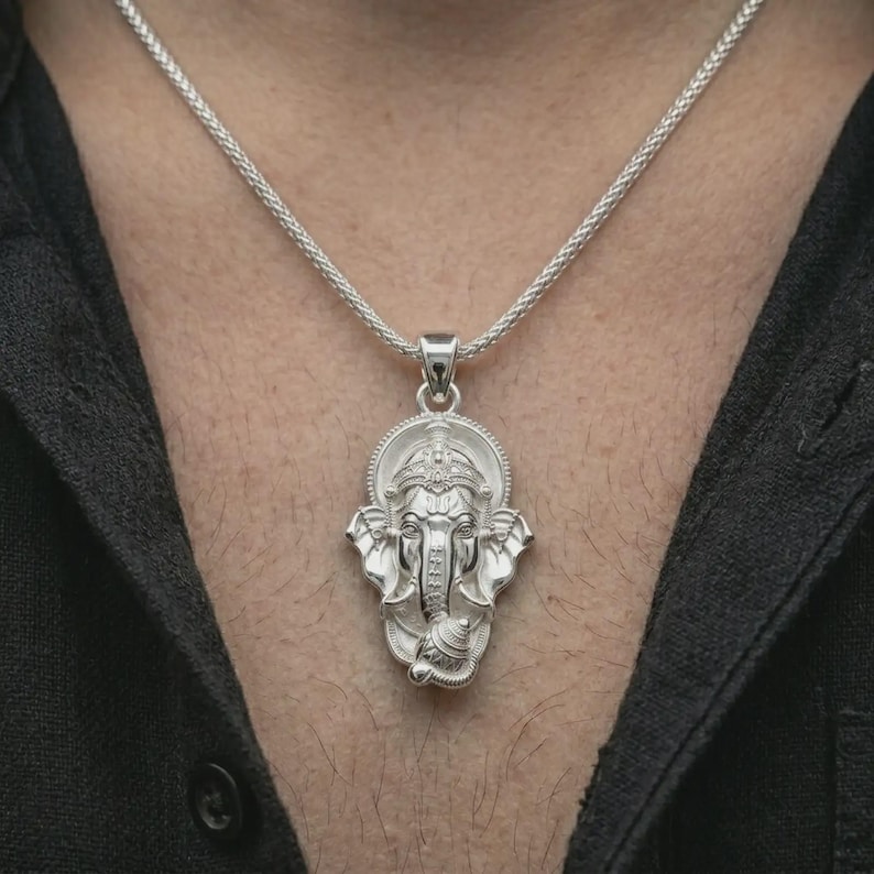 Polished silver Ganesha pendant necklace worn on the chest, masculine lifestyle shot highlighting the elephant god relief, ornate crown, and bright silver finish.