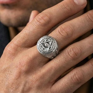 Polished silver Masonic eye-in-triangle ring on the finger, wearable macro focusing on the circular inscription and relief details