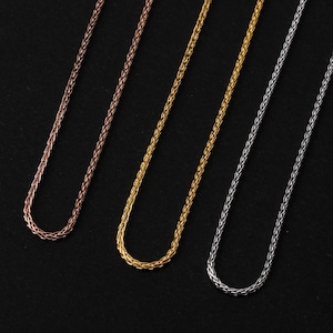 Puede incluir: Tres collares de cadena de trigo en tonos oro rosa, oro y plata se muestran sobre un fondo negro. Las cadenas tienen una textura finamente tejida. Los collares est&aacute;n dispuestos en fila, mostrando sus diferentes acabados met&aacute;licos.