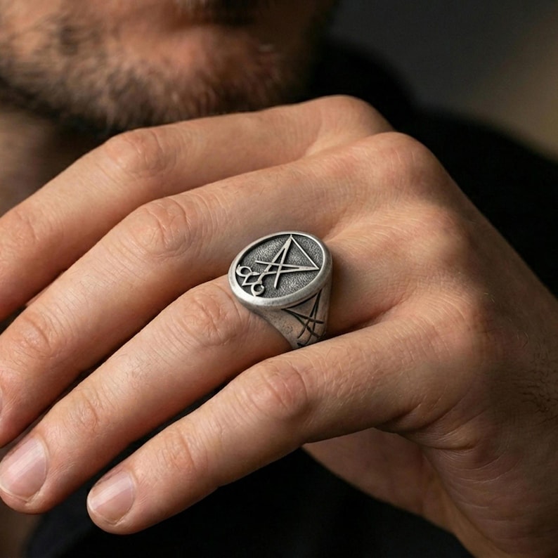 Oxidized Lucifer sigil signet ring worn on a finger, close-up lifestyle shot highlighting the raised symbol and textured face