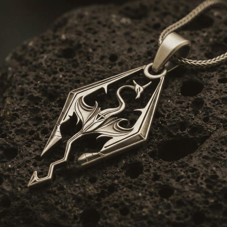 Bronze Skyrim dragon pendant necklace on textured volcanic rock, close-up studio shot highlighting the angular dragon emblem, openwork design, and antique silver contrast.