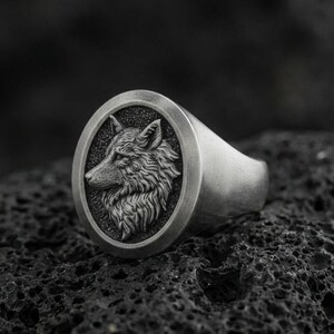 Oxidized sterling silver wolf signet ring on volcanic rock, macro closeup with deep shadow contrast
