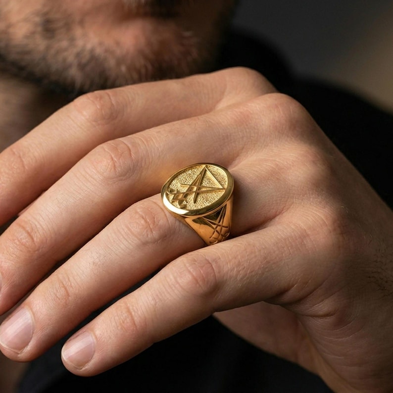 Gold plated Lucifer sigil signet ring worn on a finger, close-up lifestyle photo focusing on the raised emblem and contrast detailing
