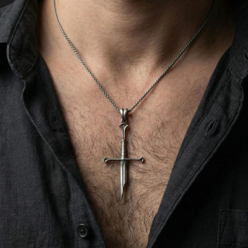 Oxidized sword pendant necklace worn on neck, lifestyle close-up on dark outfit, minimal premium studio look