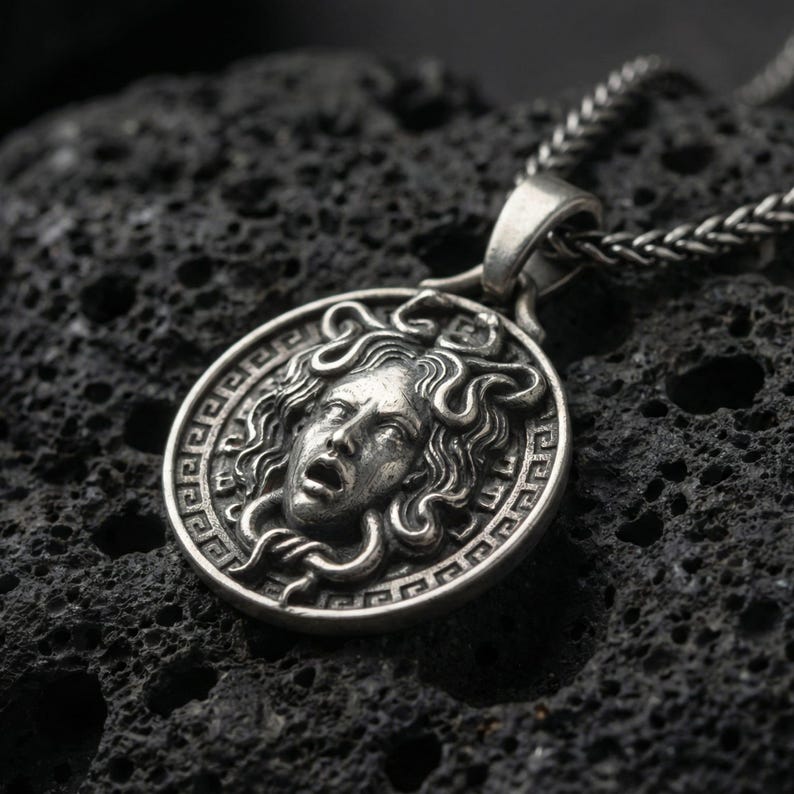 Oxidized Medusa necklace pendant photographed on volcanic rock with detailed snake hair relief and Greek key border