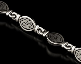 May include: Close-up of a silver bracelet with an ornate design. The bracelet features repeating oval-shaped links with a detailed, symmetrical pattern in a darker shade of silver. The links are connected by curved, scroll-like elements.