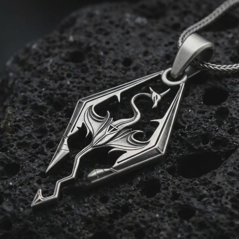 Oxidized Skyrim dragon pendant necklace on textured volcanic rock, close-up studio shot highlighting the angular dragon emblem, openwork design, and antique silver contrast.