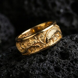 Gold plated dragon and koi fish band ring on volcanic rock, high-relief Japanese motif with engraved texture, luxury jewelry product photography.