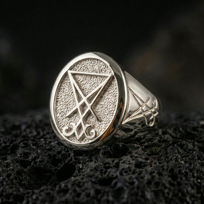 Polished silver Lucifer sigil signet ring featuring a bold raised emblem and clean beveled edges, close-up on volcanic stone