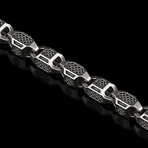 May include: A silver-colored chain necklace with a geometric design. The chain links are hexagonal with a textured pattern and rectangular cutouts. The necklace is displayed against a black background.