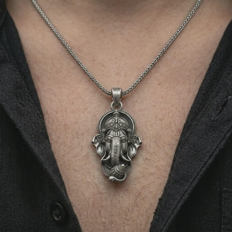 Oxidized Ganesha pendant necklace worn on the chest, close-up lifestyle jewelry photo showing the spiritual talisman on a spiga chain with dark clothing.