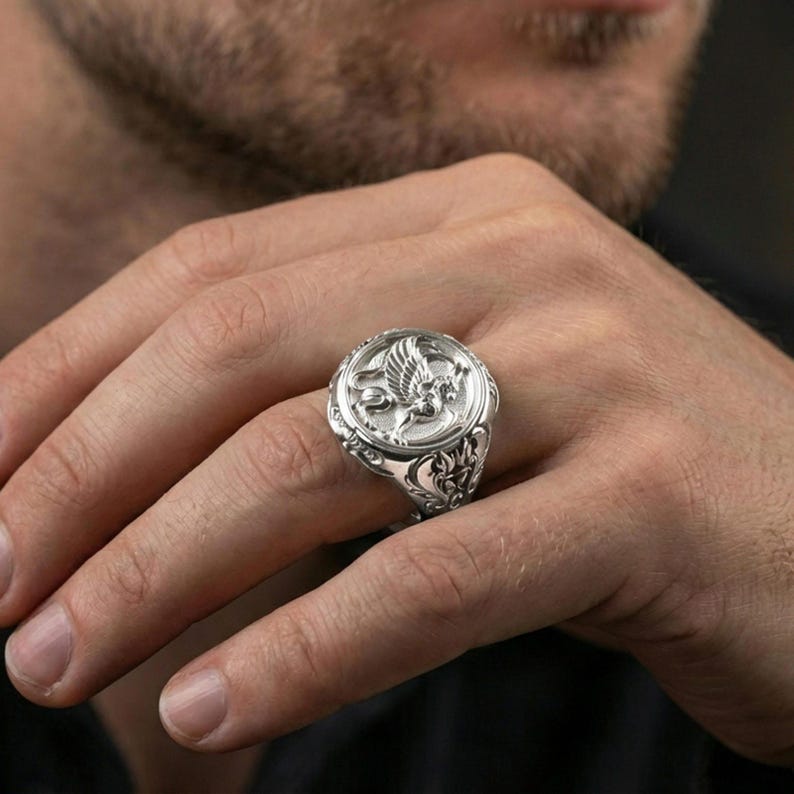 Polished silver griffon ring on finger highlighting detailed griffin relief and ornamental frame, clean lifestyle wear photo
