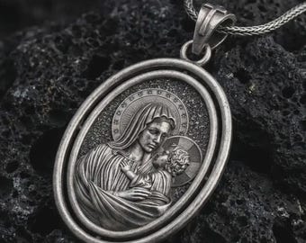 May include: Silver-toned oval pendant necklace featuring a detailed relief of Mary holding baby Jesus. The pendant is suspended from a matching chain. The background is a dark, textured surface.