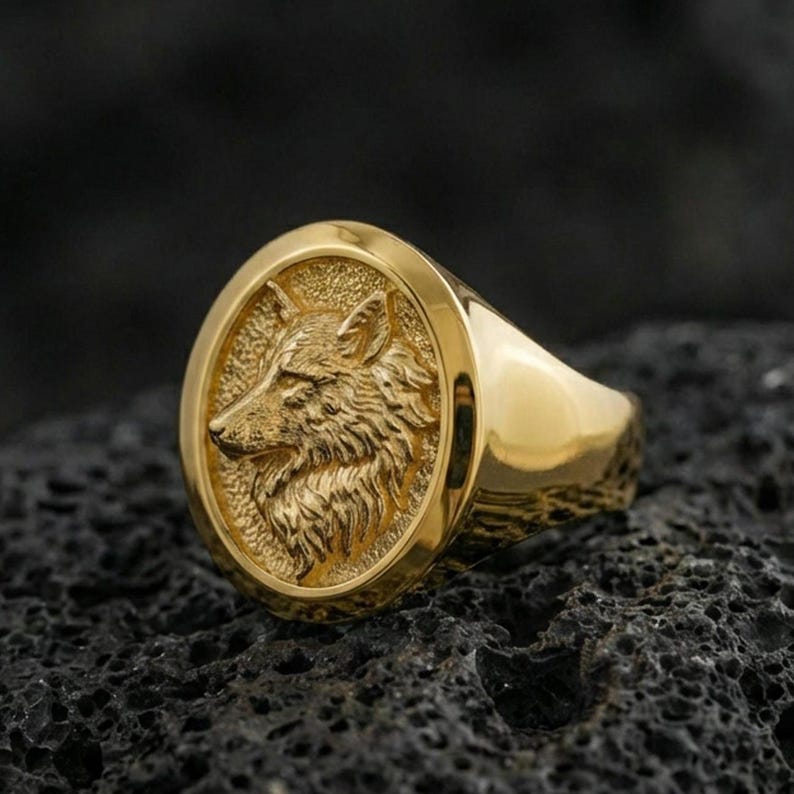 Gold plated wolf head ring on volcanic stone, bold animal emblem with crisp sculpted fur texture