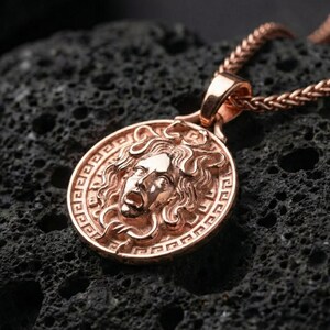 Rose gold plated Medusa mythology pendant presented on volcanic rock surface with dark classical aesthetic