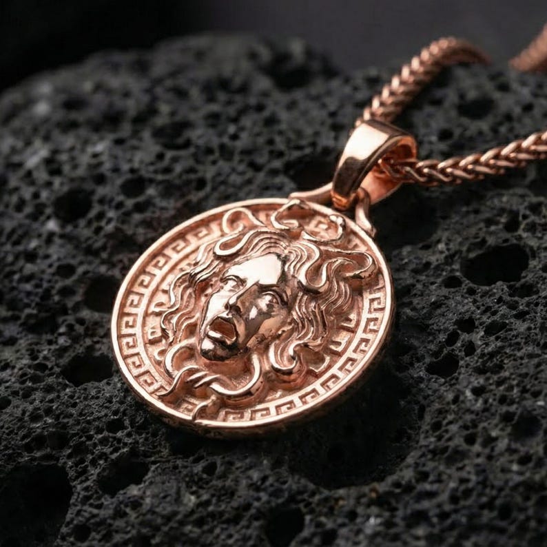 Rose gold plated Medusa mythology pendant presented on volcanic rock surface with dark classical aesthetic