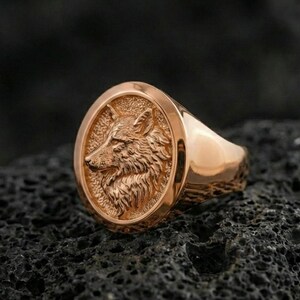 Rose gold plated wolf signet ring on volcanic rock, detailed wolf profile with luxury warm metal tone