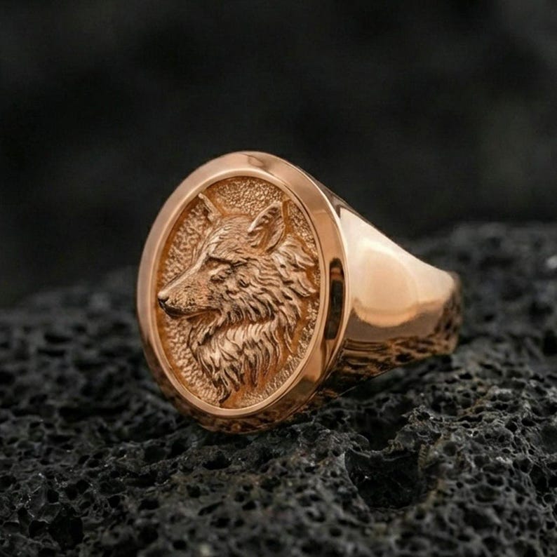Rose gold plated wolf signet ring on volcanic rock, detailed wolf profile with luxury warm metal tone
