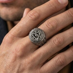 Oxidized all-seeing eye triangle ring worn on a finger, close-up lifestyle photo highlighting the engraved Latin motto
