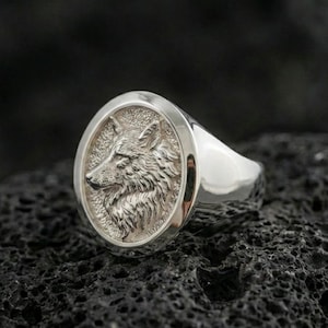 Polished silver wolf head ring on volcanic stone, clean profile carving and premium studio lighting