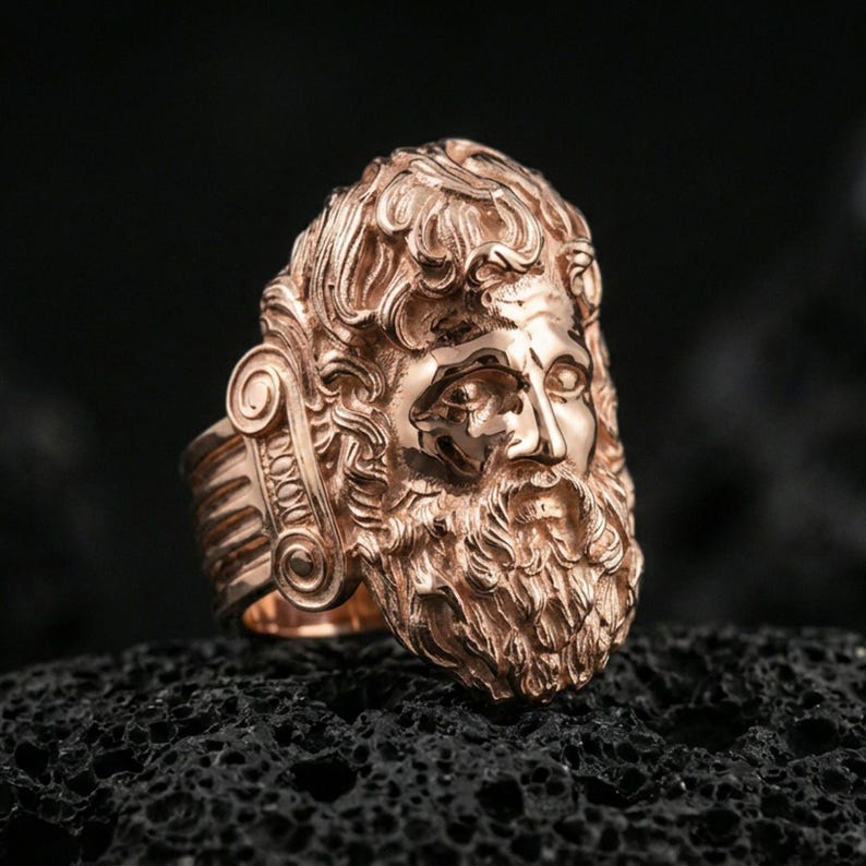 Rose gold plated Zeus ring showcasing expressive god face sculpture and rich texture, sharp close-up product photography on volcanic rock
