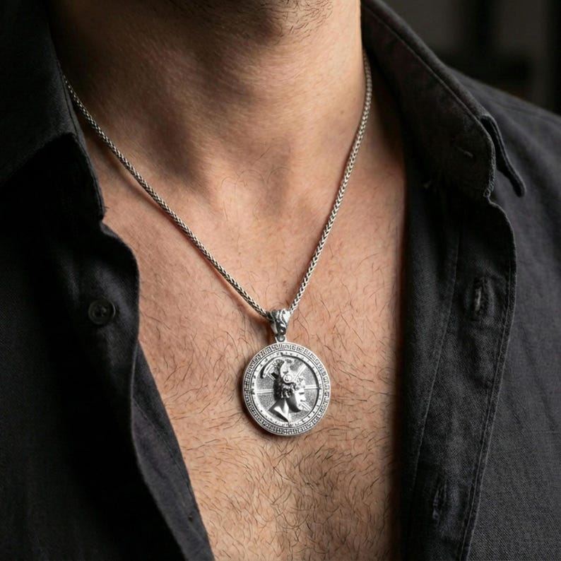 Polished silver Perseus coin pendant necklace worn on the neck, clean lifestyle wear shot capturing bright shine and the detailed winged helmet relief in natural light.