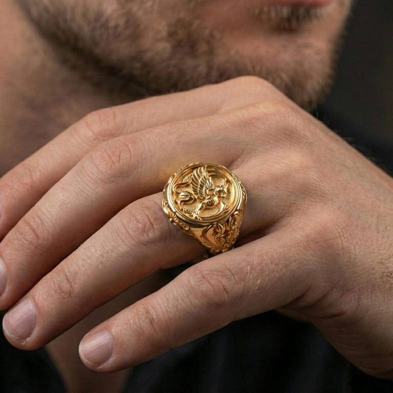 Gold plated griffon signet ring worn on finger, statement fantasy jewelry inspired by ancient mythical guardians, premium lifestyle close-up