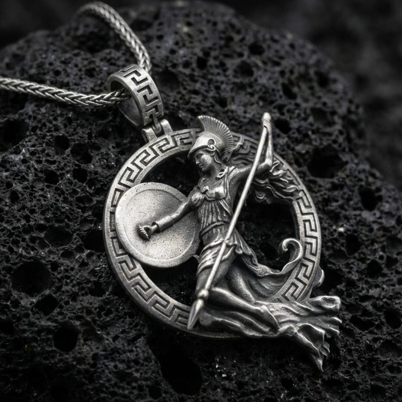 Oxidized Athena warrior pendant necklace on textured volcanic rock, centered close-up highlighting the Greek key frame, helmeted goddess figure, spear, and deep antique shadowed contrast.