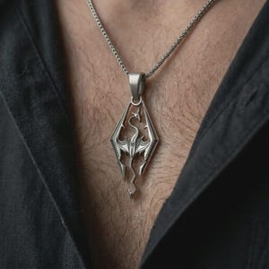 Oxidized Skyrim dragon pendant necklace worn on the chest, close-up lifestyle jewelry photo showing the fantasy emblem pendant on a spiga chain with dark clothing.