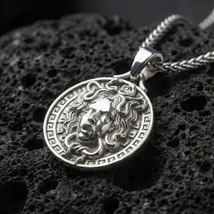Polished silver Medusa Greek mythology pendant displayed on volcanic stone background with sharp sculpted facial detail