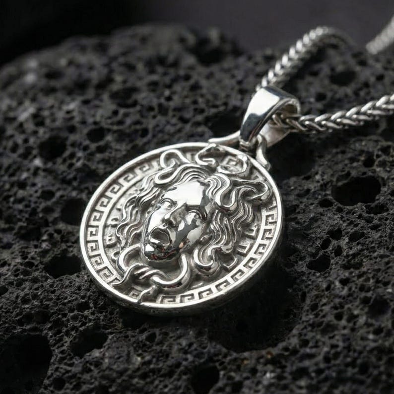 Polished silver Medusa Greek mythology pendant displayed on volcanic stone background with sharp sculpted facial detail