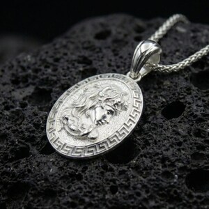 Polished silver Medusa necklace on porous volcanic stone, Greek key frame coin pendant with detailed relief portrait and vintage texture