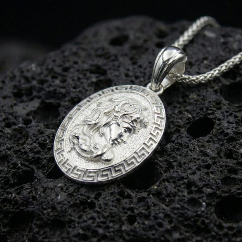 Polished silver Medusa necklace on porous volcanic stone, Greek key frame coin pendant with detailed relief portrait and vintage texture