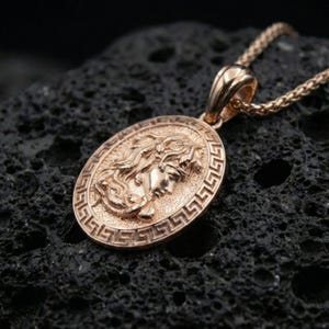 Rose gold plated Medusa necklace on dark volcanic stone, Greek key coin pendant with sculpted Medusa profile and antique-inspired finish