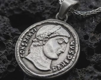 May include: Silver-colored pendant necklace featuring a detailed coin design. The coin depicts a profile of a person with the inscription "CONSTANTIVS" and other text. The pendant hangs from a silver chain.