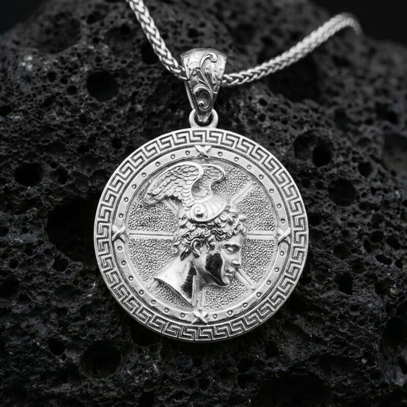 Polished silver Perseus coin pendant necklace on textured volcanic rock, crisp macro product photo emphasizing clean edges, sharp engraving, and bright reflective highlights on the portrait and border.